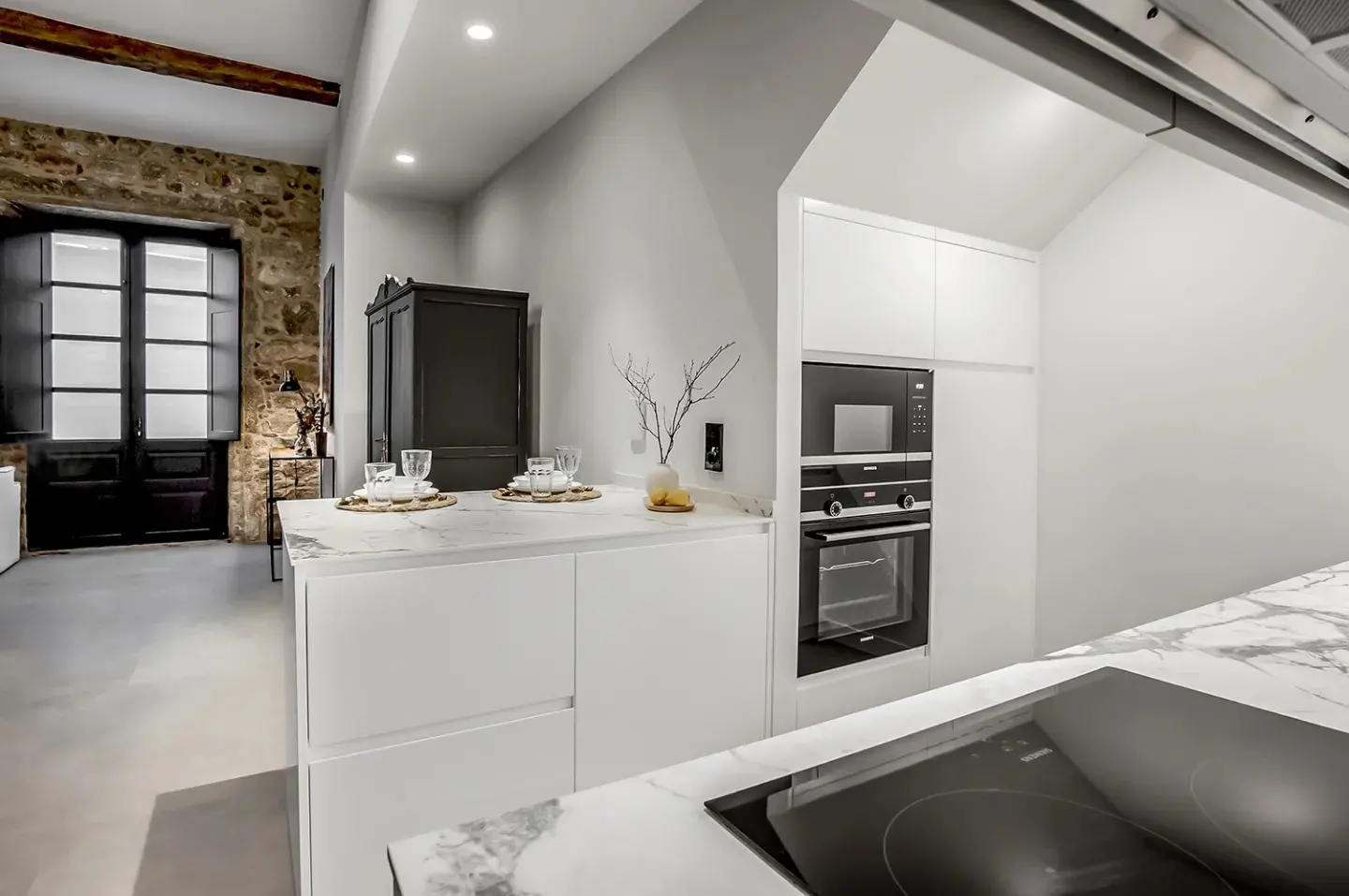 La cocina blanca, con horno en columna, junto al muro de piedra y la carpintería restaurada