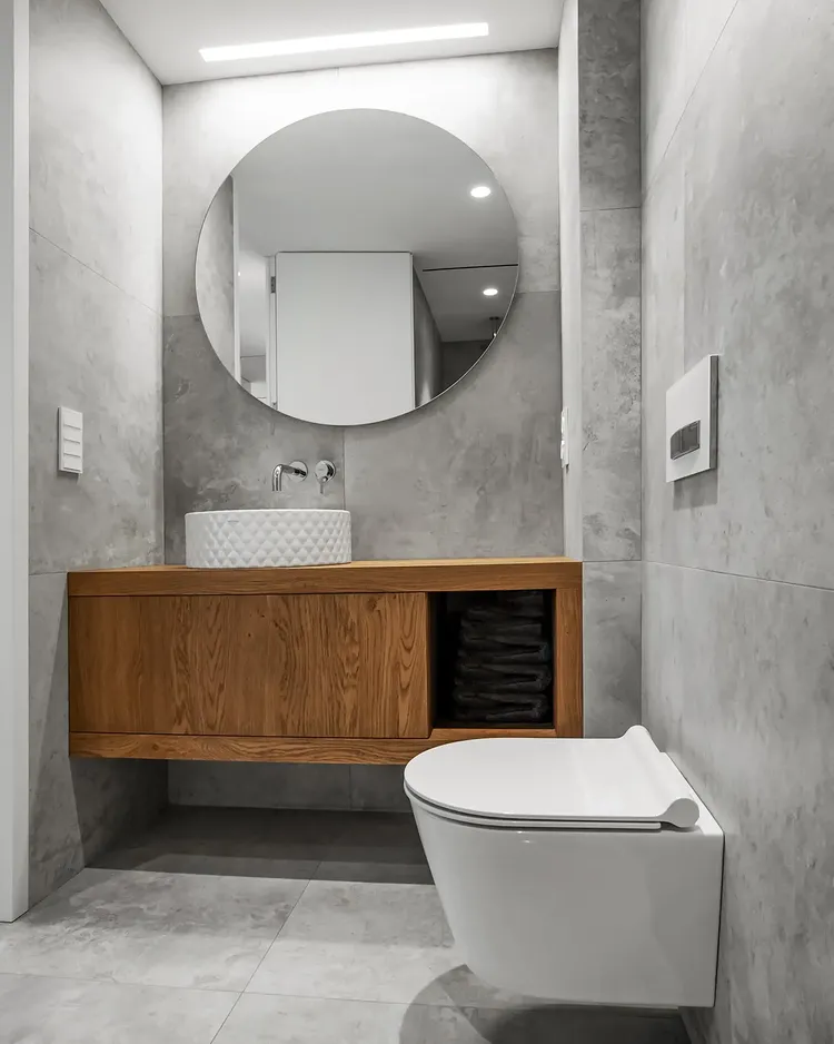 Aseo con lavabo texturizado sobre mueble de roble y espejo redondo